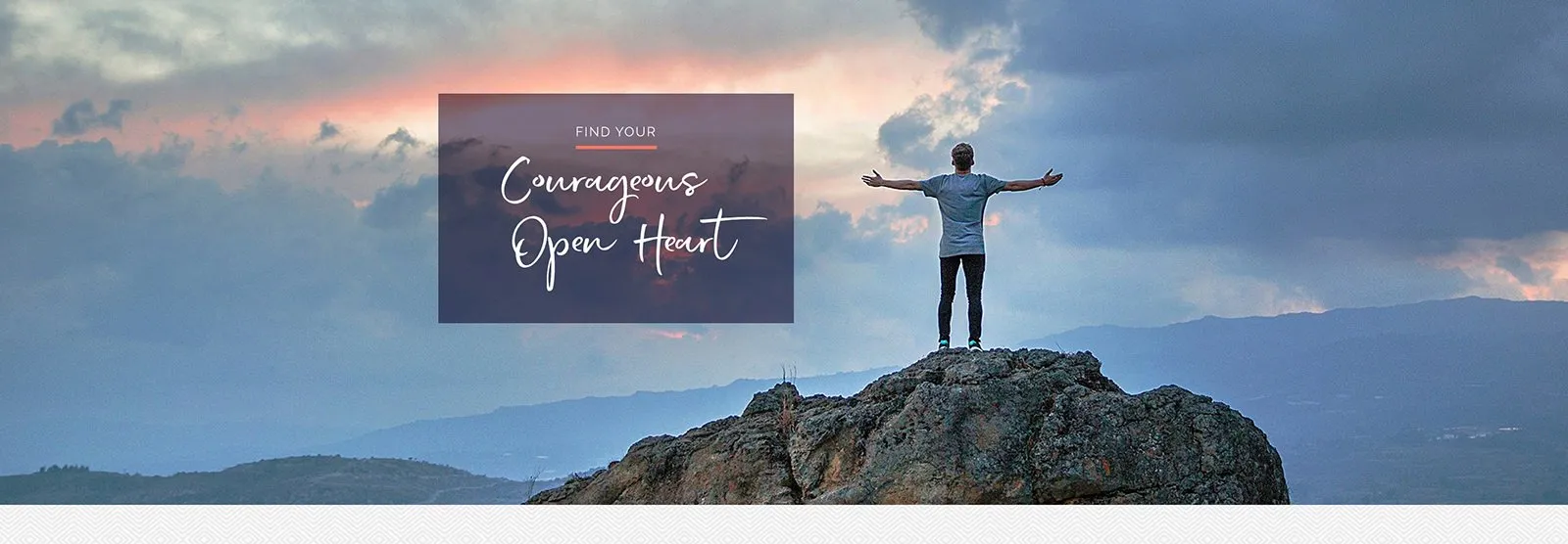 A person on a rocky summit with arms wide open under a pink sky. Text on the photo reads: Find your courageous open heart.